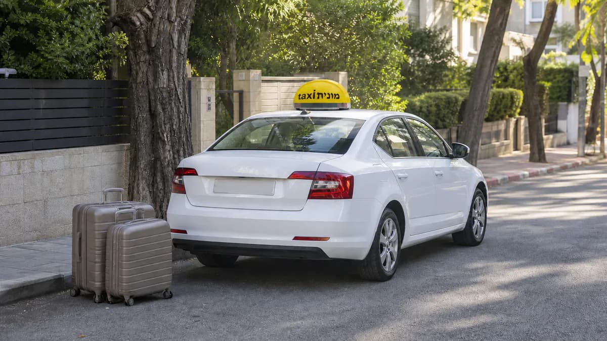 מונית לבנה עם כובע צהוב ועליו הכיתוב מונית taxi ומזוודות לקראת יציאה מתל אביב־יפו